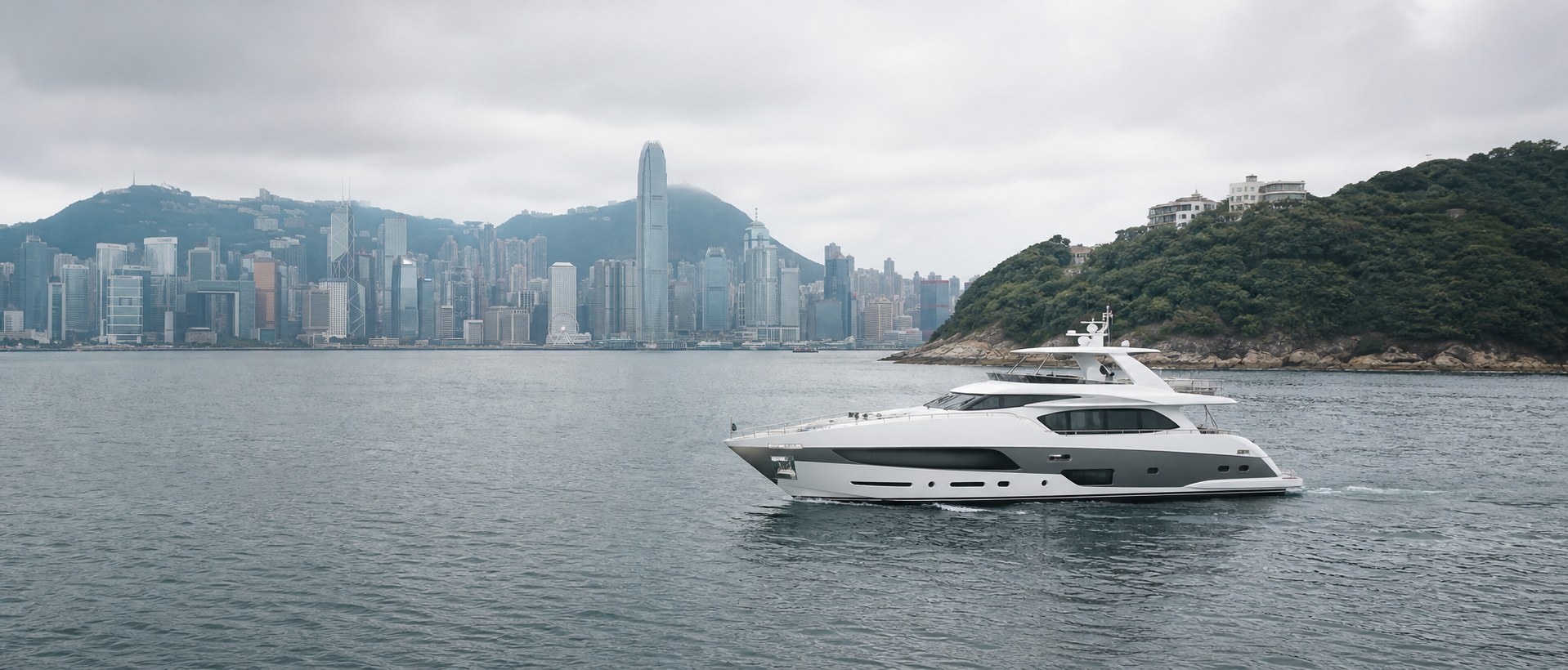 遊艇在香港島海岸及維港背景前航行，適合作為大灣區遊艇流動文章配圖
